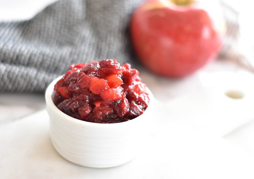 White bowl filled with AIP, paleo apple cranberry sauce next to an apple.