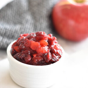 White bowl filled with AIP, paleo apple cranberry sauce next to an apple.