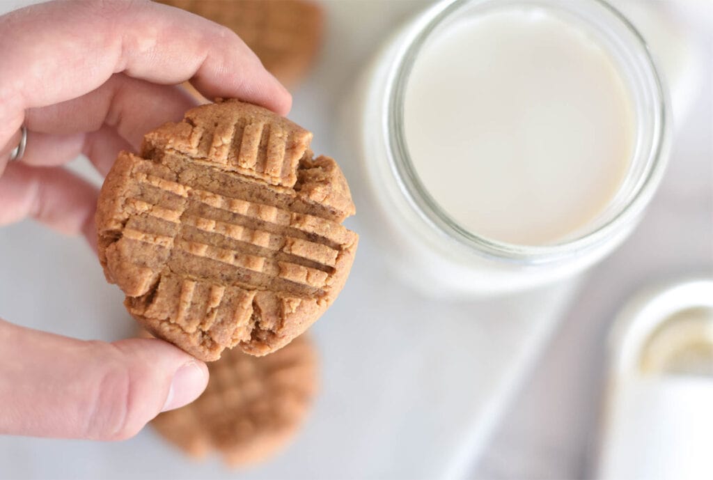 Hand holding keto peanut butter cookie over glass of milk.