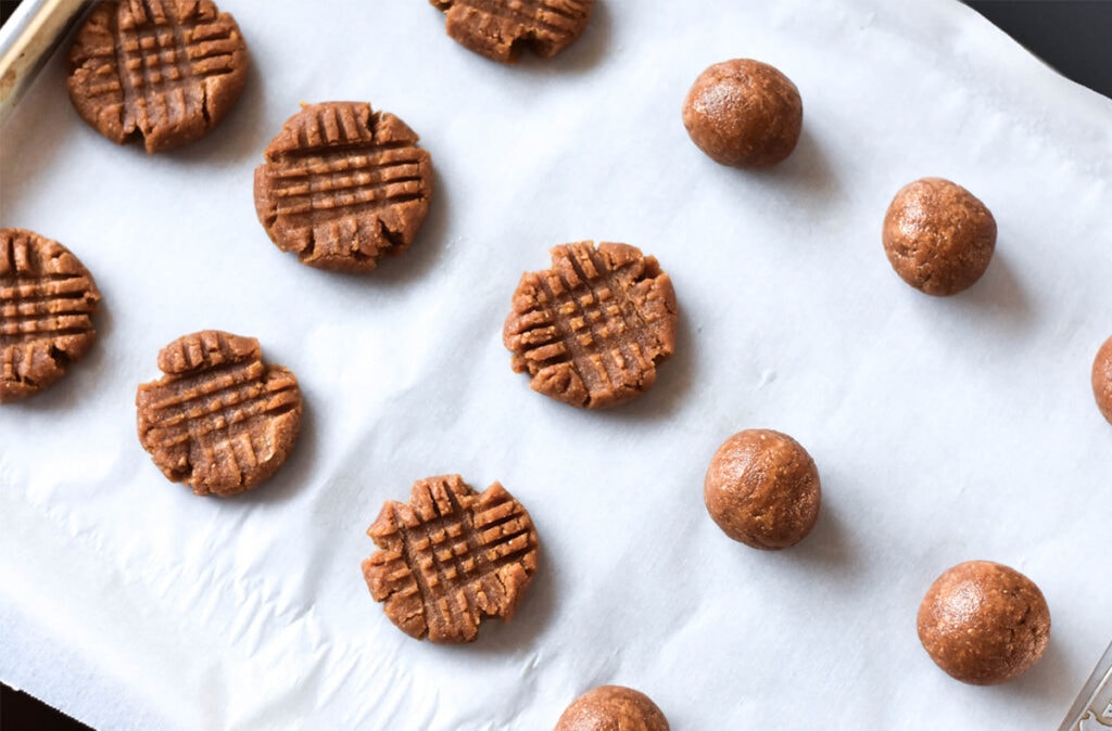 Sheet pan lined with rolled cookie dough, some balls have been crosshatched with a fork.