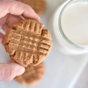 Hand holding keto peanut butter cookie over glass of milk.