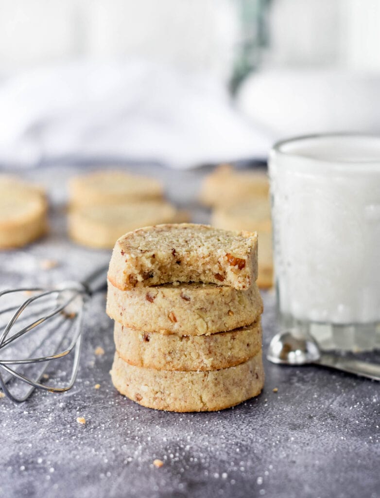 Stack of 4 keto pecan sandies, one with a bite out of it next to a glass of milk.