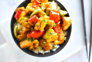 Close up shot of a dark bowl with brightly colored chicken and bell peppers on a bed of rice.