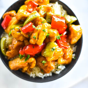 Close up shot of a dark bowl with brightly colored chicken and bell peppers on a bed of rice.