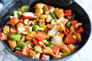 Cast iron skillet with cashew chicken stir fry, bell peppers and onions.