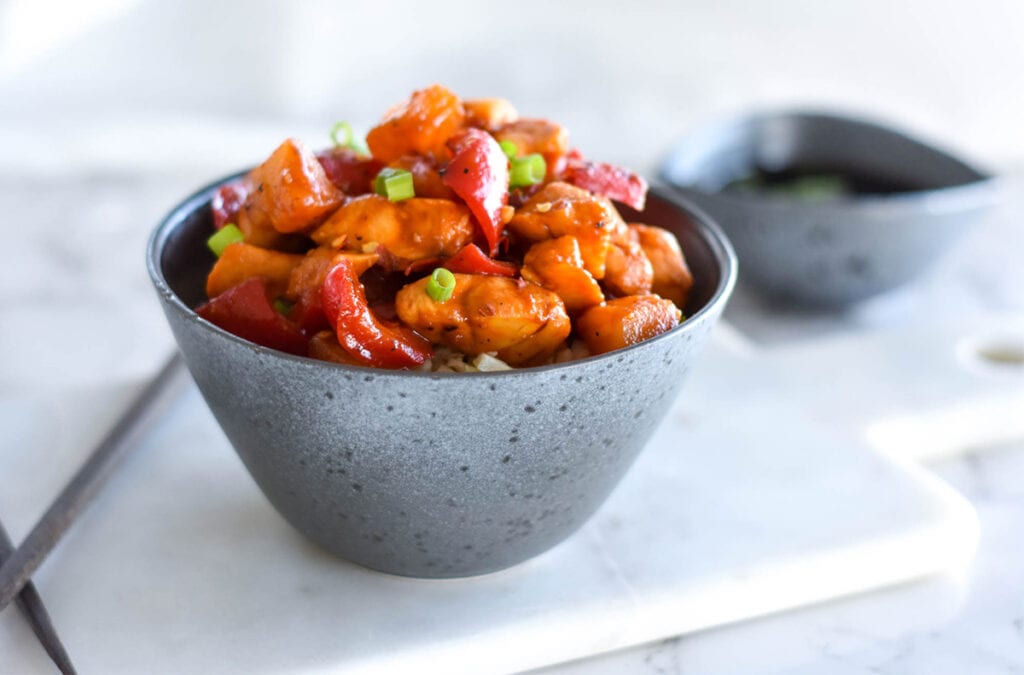 Stoneware bowl filled with paleo pineapple chicken topped with green onions.