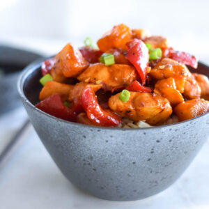 Stoneware bowl filled with paleo whole30 pineapple chicken topped with green onions.