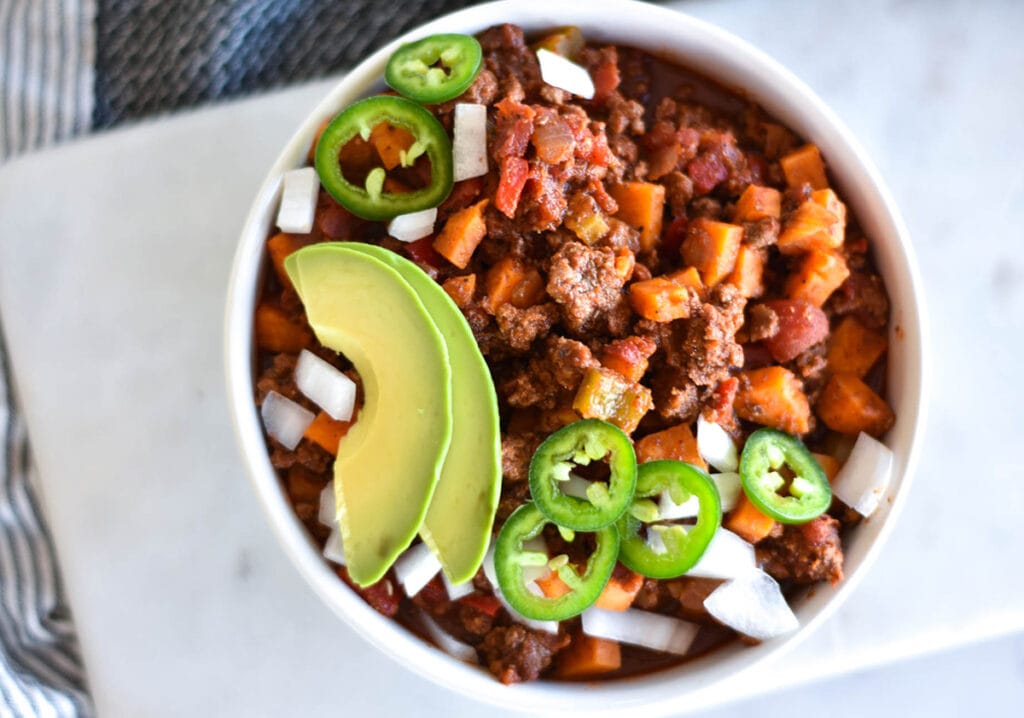 Whole30 paleo sweet potato chili topped with avocado and jalapenos in a white bowl.