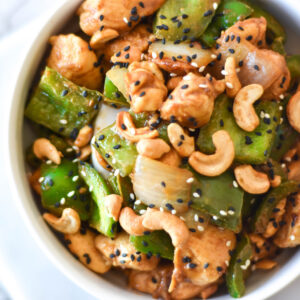 Bowl of chicken with green bell peppers, onions, cashews and black sesame seeds.