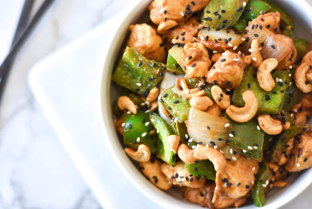 Bowl of chicken with green bell peppers, onions, cashews and black sesame seeds.