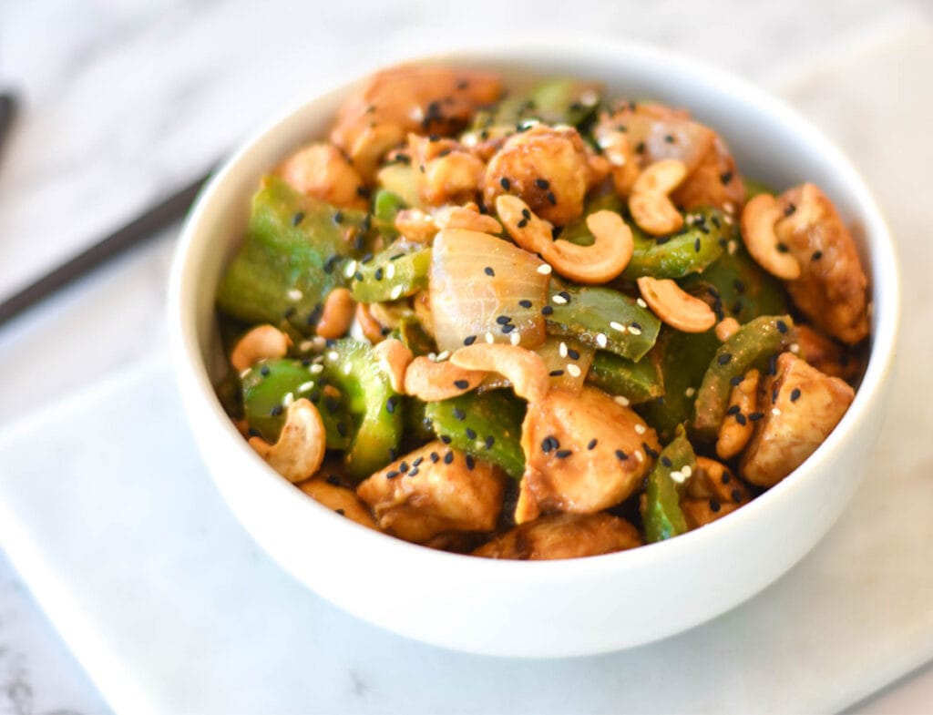 Bowl of cashew chicken stir fry with green bell peppers, onions, cashews and black sesame seeds.