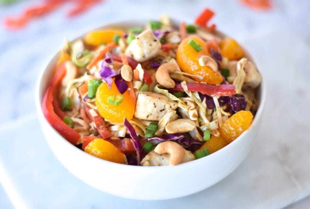 Bowl of Paleo Asian Chicken Salad with brightly colored mandarin oranges, bell peppers, green onions, cabbage and cashews.
