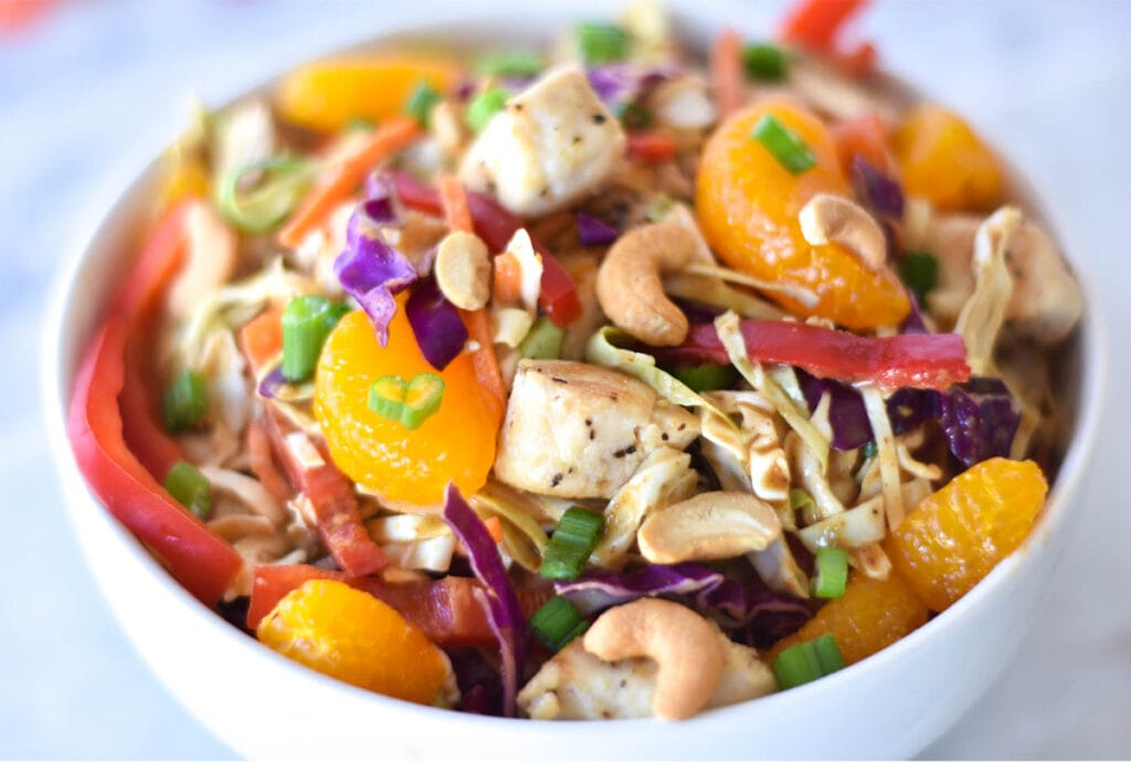 Bowl of Whole30 Asian Chicken Salad with brightly colored mandarin oranges, bell peppers, green onions, cabbage and cashews.