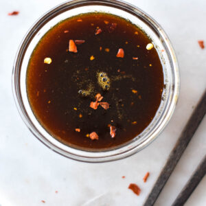 Clear dish full of paleo teriyaki sauce next to a set of chopsticks.