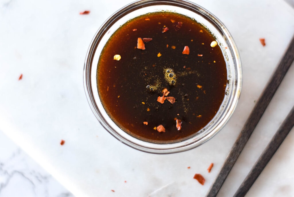 Clear dish full of AIP teriyaki sauce next to a set of chopsticks.