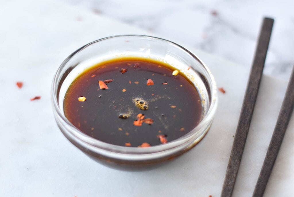 Clear dish full of paleo teriyaki sauce next to a set of chopsticks.