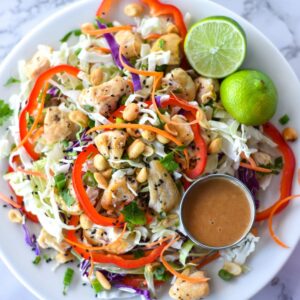 Large spicy Thai chicken salad with red bell pepper, green and purple cabbage, chicken, peanuts and carrots.