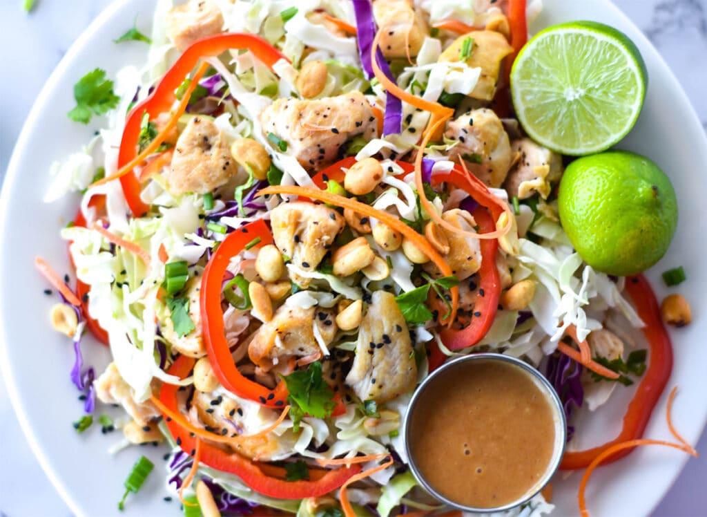 Large spicy Thai chicken salad with red bell pepper, green and purple cabbage, chicken, peanuts and carrots.