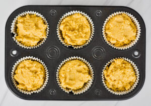 tray of unbaked cornbread muffins demonstrating that the muffin liners are filled comepletly.
