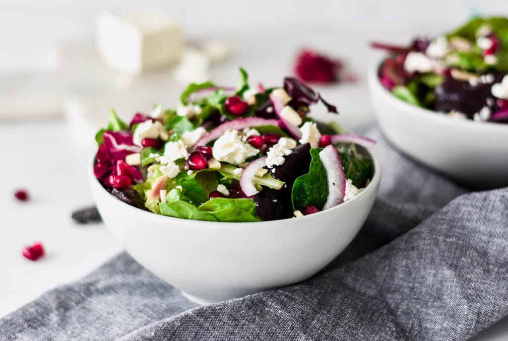 Brightly colored bowls of salad with feta, slivered almond, pomegranate seeds and mixed greens.