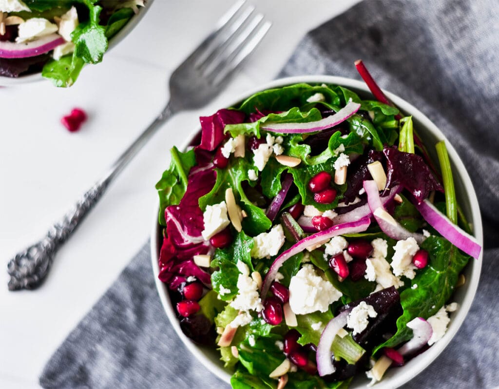 Brightly colored bowls of winter salad with feta, slivered almond, pomegranate seeds and mixed greens.