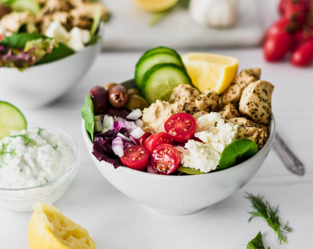 Low Carb Greek Chicken Bowls with cucumber, red onion, cherry tomatoes, Greek chicken hummus, feta and tzatziki.