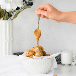 Hand dripping peanut butter on a bowl of protein balls.