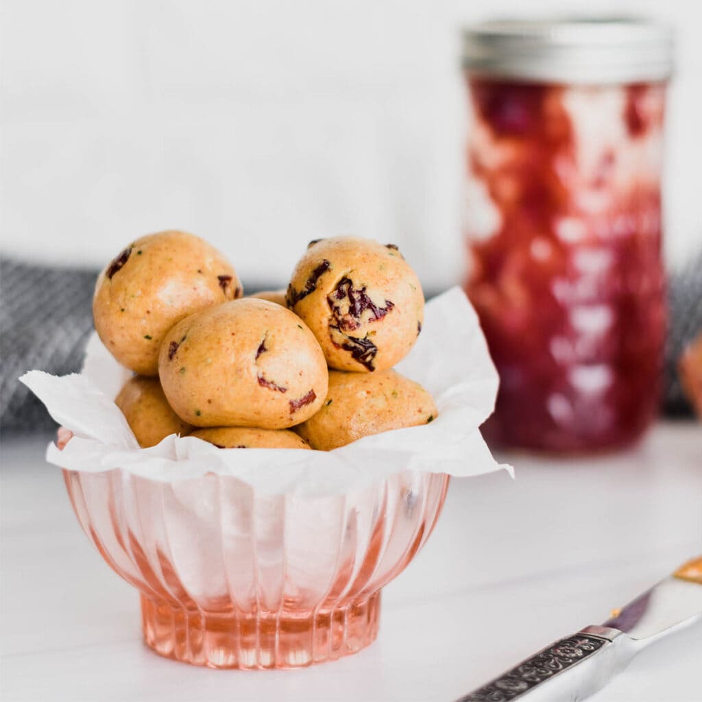 Bowl of peanut butter and jelly protein balls with jelly jar in background.