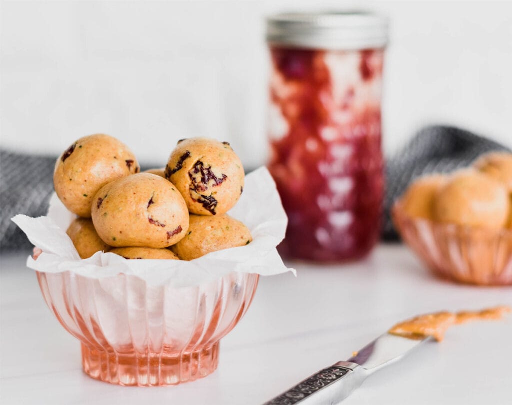 Bowl of peanut butter and jelly protein balls with jelly jar in background.