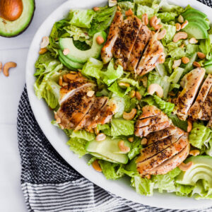 Brightly colored Whole30 Caesar Salad with green romatine lettuce, avocado and chicken.