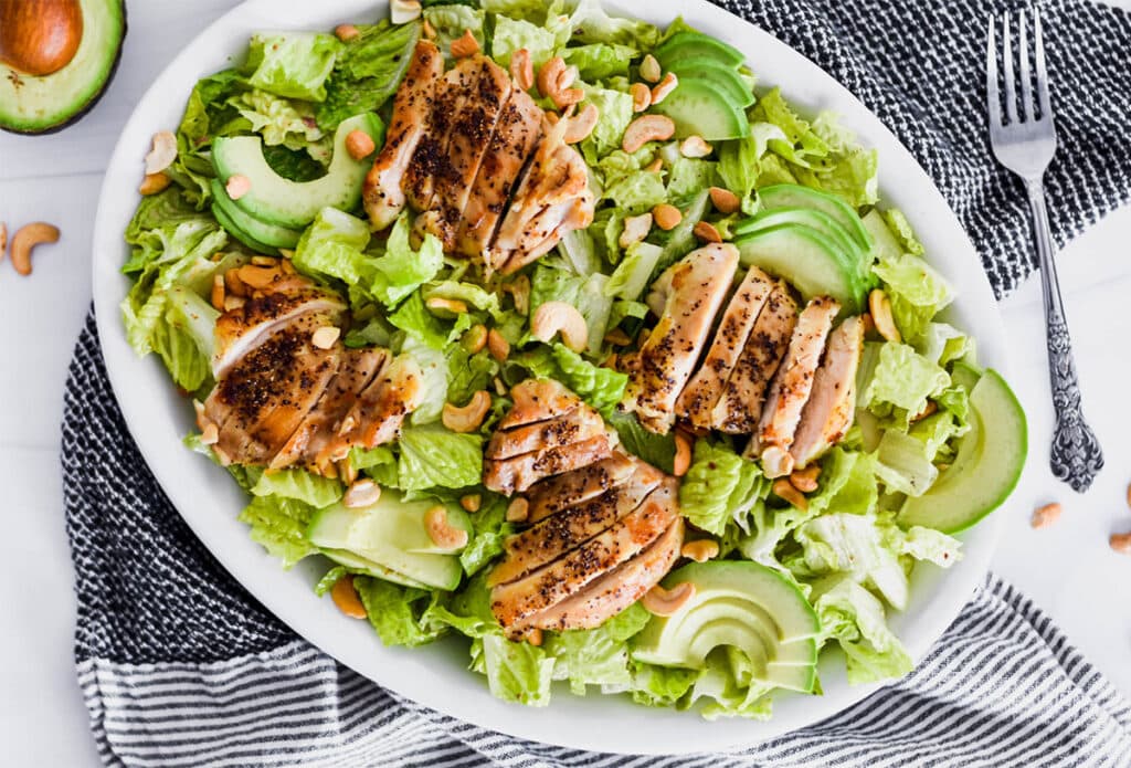 Brightly colored plate of green romatine lettuce, avocado and chicken.