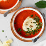 Bowl of brightly colored, red keto tomato soup topped with basil and melty cheese.