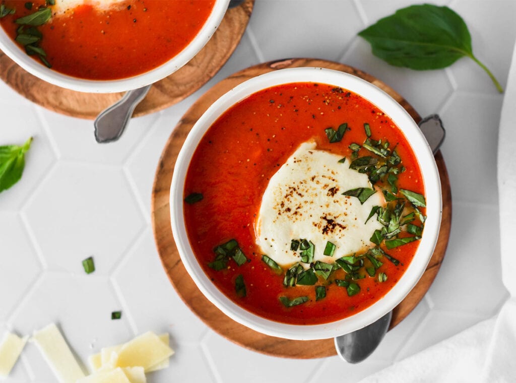 Bowl of brightly colored, red keto tomato soup topped with basil and melty cheese.