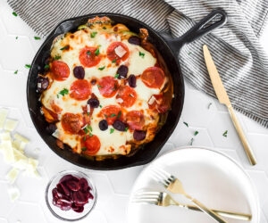 Cast iron skillet loaded with chicken breast and pizza toppings, covered in melted cheese.