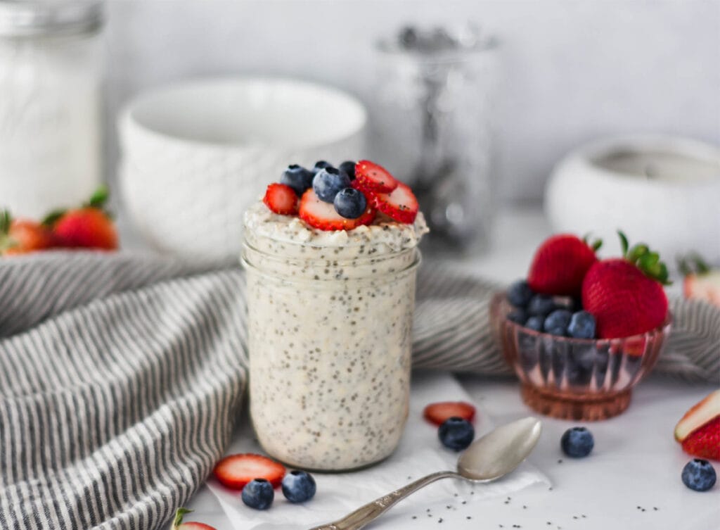 Mason jar overfilled with overnight oats topped with strawberries, blue berries and chia seeds.