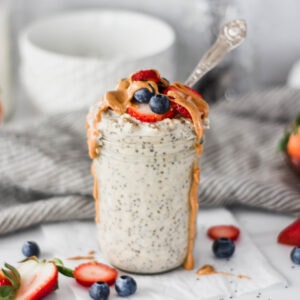 Mason jar overfilled with protein overnight oats topped with strawberries, blue berries and dripping peanut butter.