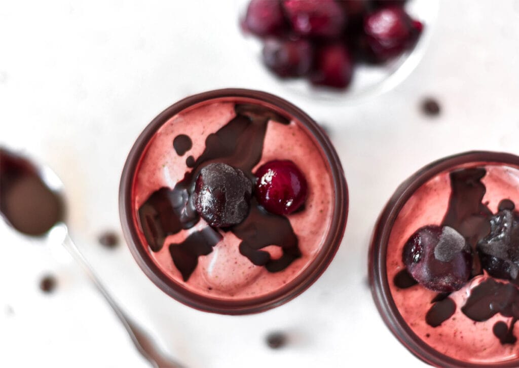 Red smoothie with cherries and hard chocolate sauce on top.