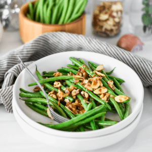 White plate filled with bright green green beans with almonds and shallot.