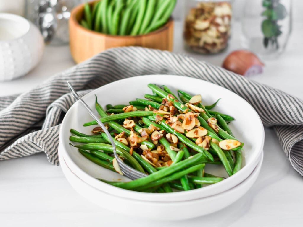 White plate filled with bright green green beans with almonds and shallot.