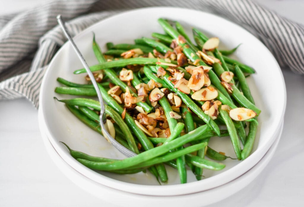 White plate filled with bright green whole30 green beans with almonds and shallot.