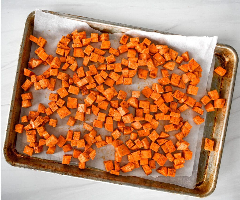 Diced sweet potato on a parchment sheet lined baking sheet, uncooked.