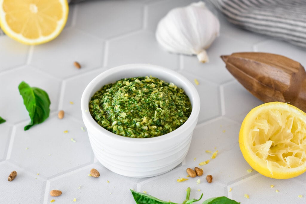 White dish filled with bright green pesto with lemon zest.