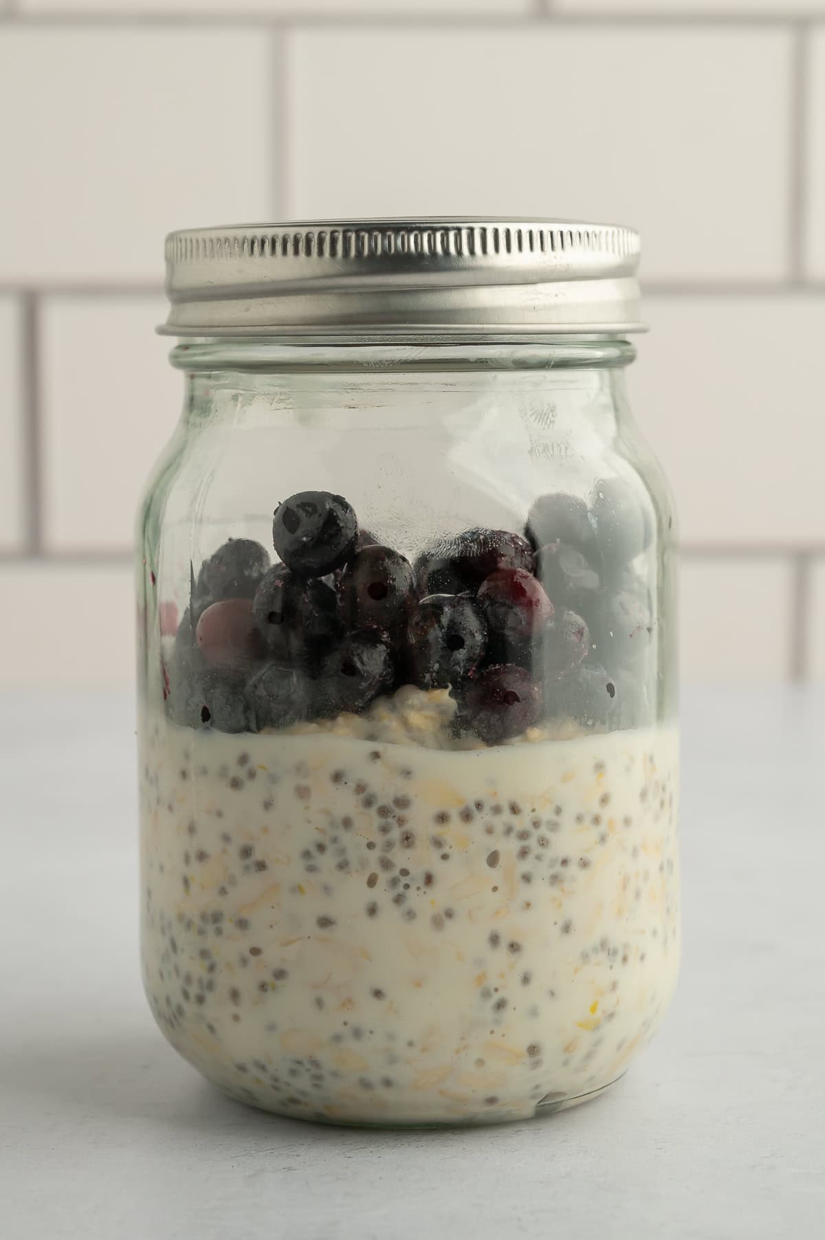 Jar of set lemon overnight oats topped with frozen blueberries.