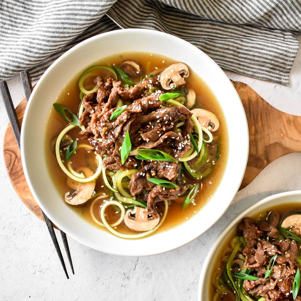 Bowl of bone broth with zucchini noodles, mushrooms, green onions and bulgogi.