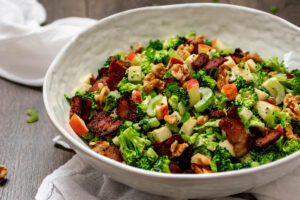 Bowl full of chopped broccoli salad with celery, apple, walnuts and bacon.