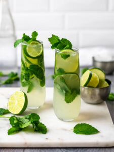 Two glasses of low carb mojitos filled garnished with lime and mint.