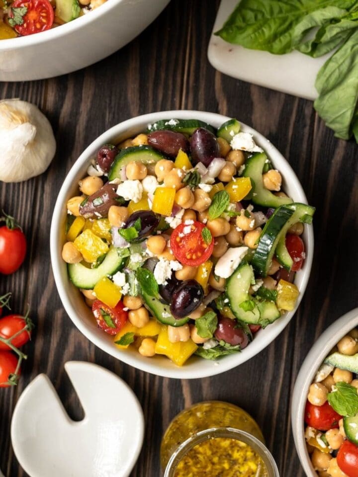 Bowl of chickpea salad with feta, olives bright red cherry tomatoes and cucumber.