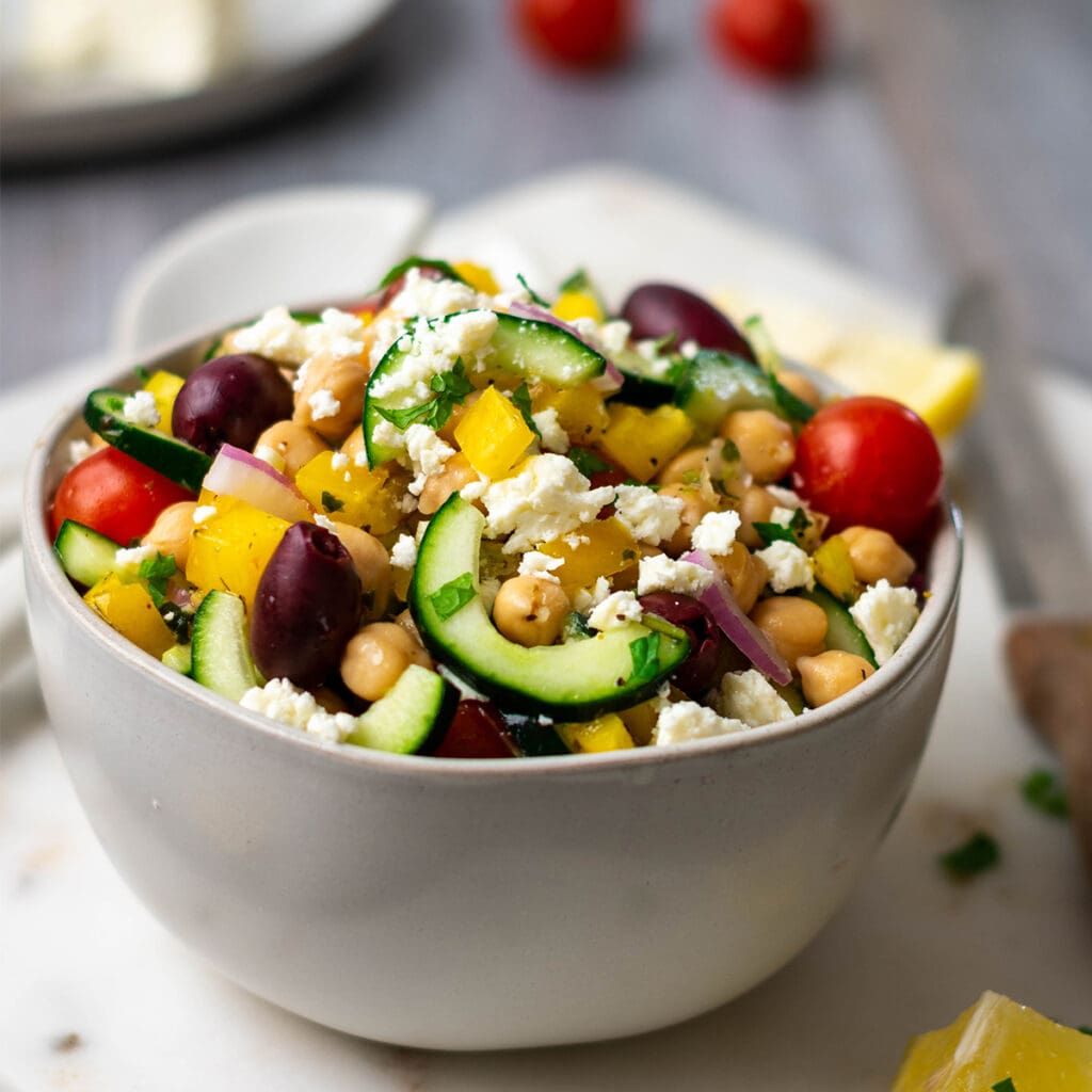 Bowl of greek salad with tomato, chickpeas, cucumber, olives, red onion, bell pepper and feta.