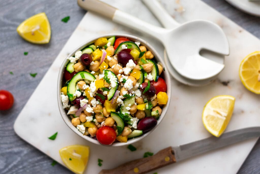 Bowl of Greek chickpea salad with cherry tomatoes, cucumber, olives, red onion, bell pepper and feta.