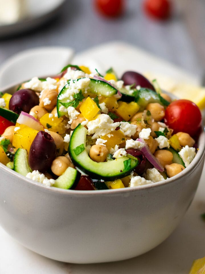 Bowl of greek salad with tomato, chickpeas, cucumber, olives, red onion, bell pepper and feta.
